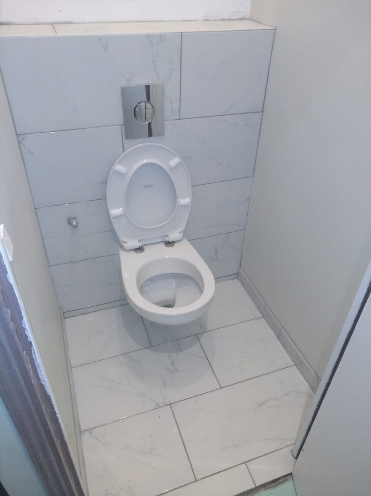 WC suspendu avec plaque de commande chromée et carrelage effet marbre